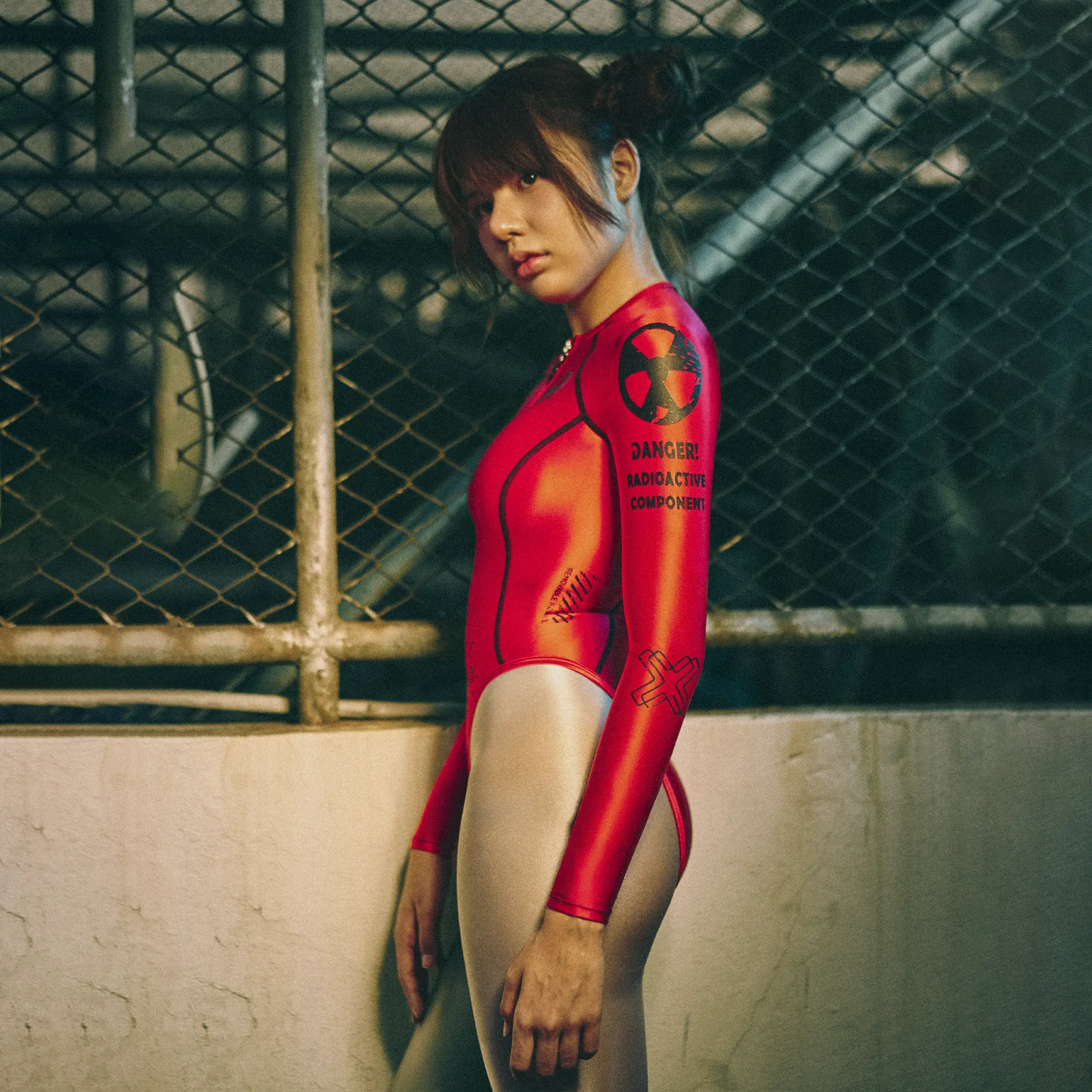 Side view of red Neoskin leotard with black hazard print on sleeve, chain-link fence behind